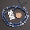 Blue kyanite beads on a string with a coin for scale on a dark background