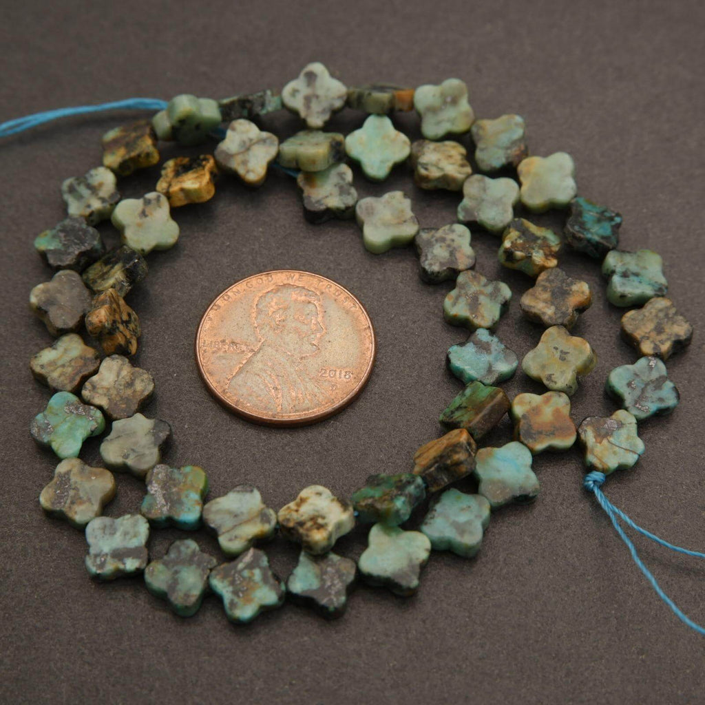 String of greenish-blue flower-shaped beads with a penny for scale on a brown background