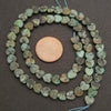 Heart-shaped turquoise beads with a penny for scale on a dark background