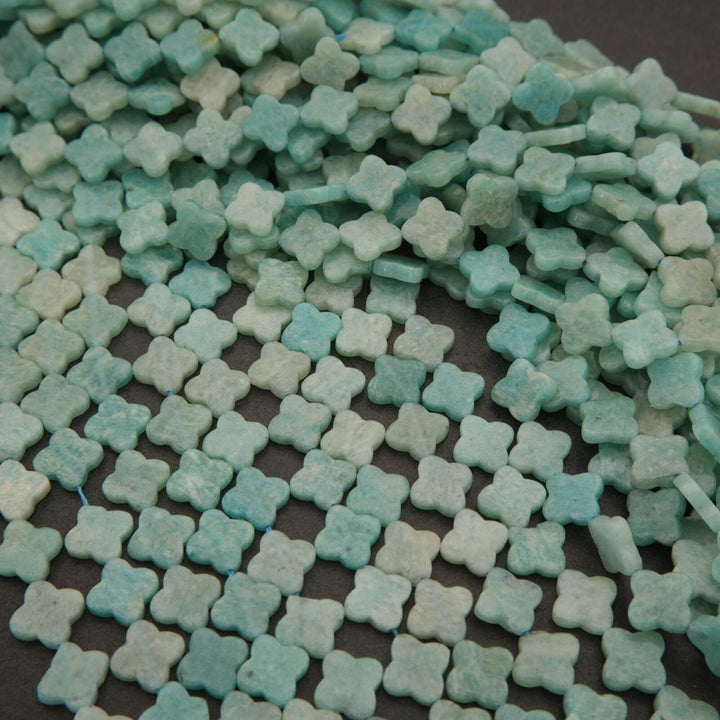 Close-up of small clover-shaped blue and green beads on a dark surface