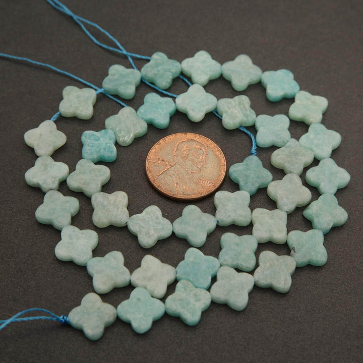 String of light blue flower-shaped beads with a penny for scale on a dark background