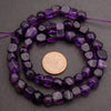 Purple beaded necklace with a coin for scale on a gray background