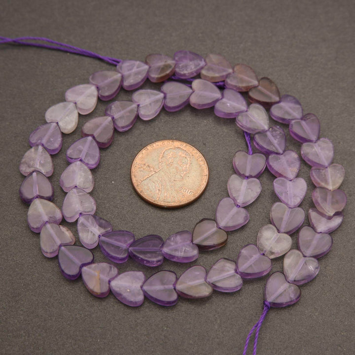 Purple heart-shaped beads on a string with a coin for size comparison on a gray background