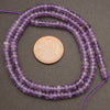 Purple beads on a string with a penny for size comparison on a gray background