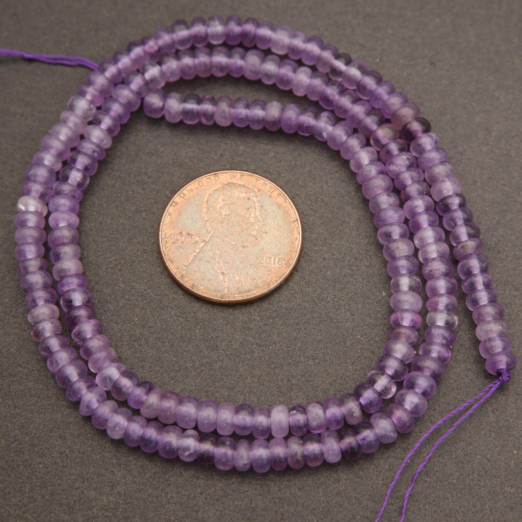 Purple beads on a string with a penny for size comparison on a gray background
