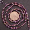 String of purple beads with a coin for size comparison on a dark background