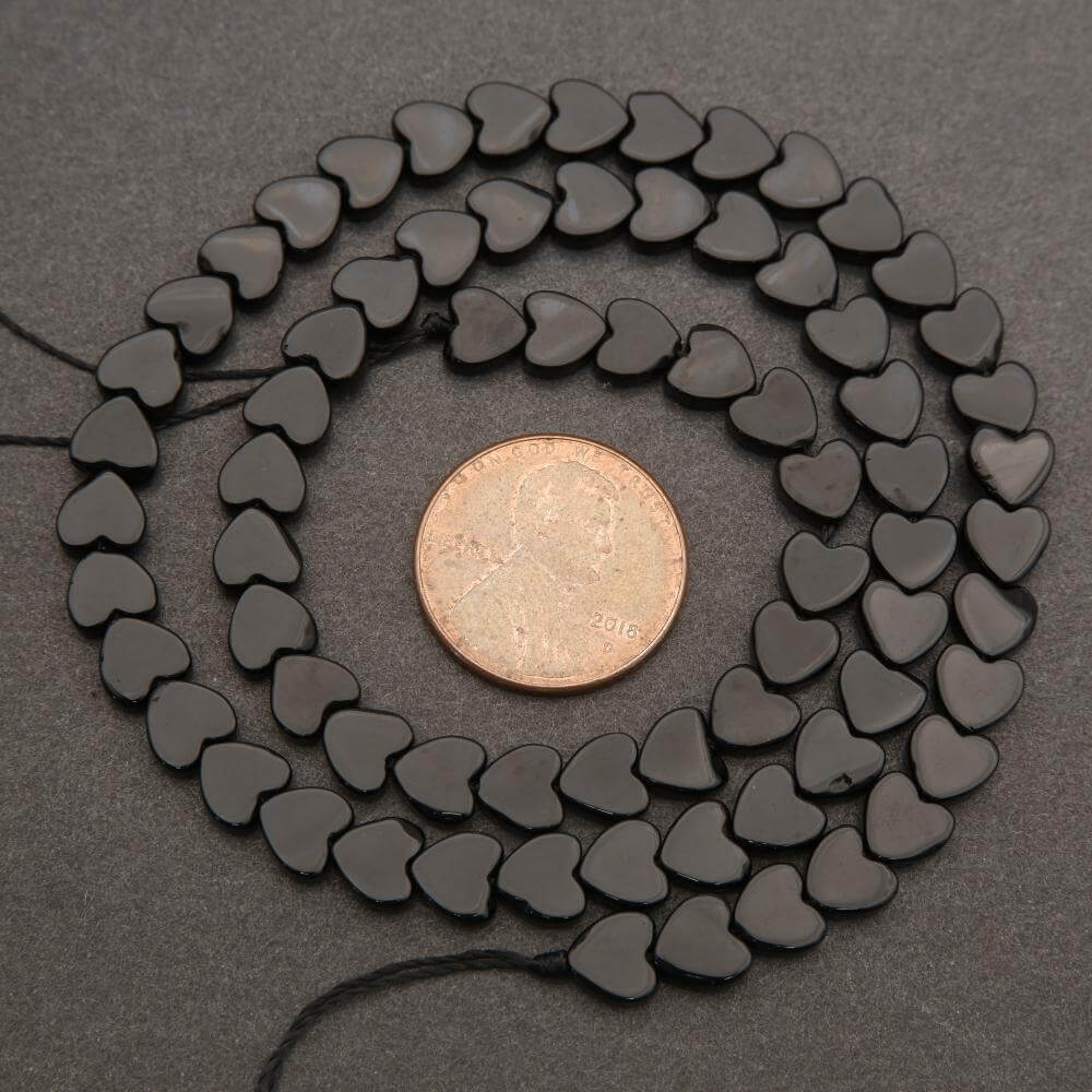 String of black heart-shaped beads with a penny for scale on a dark surface