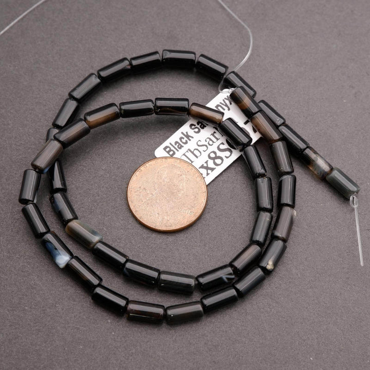 Black beaded necklace with a coin for scale on a gray background