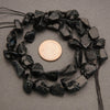 Black stone beads with a penny for scale on a gray background