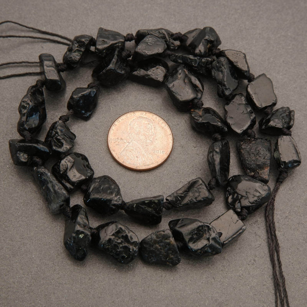 Black stone beads with a penny for scale on a gray background