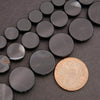 Black circular stones on a dark surface with a coin for scale