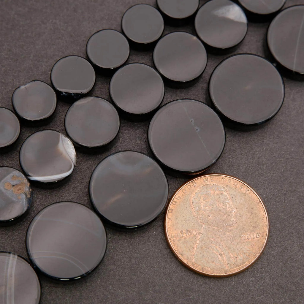 Black circular stones on a dark surface with a coin for scale