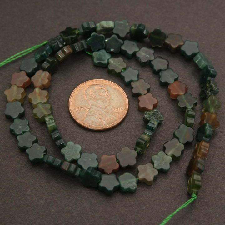 Star-shaped green beads on a string with a penny for scale on a dark surface
