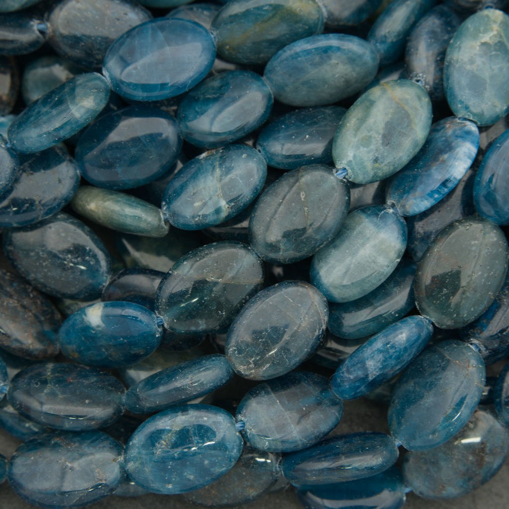 Polished blue apatite oval beads strand with natural blue color variation on a dark background.