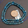 String of blue faceted beads with a coin for scale on a gray background