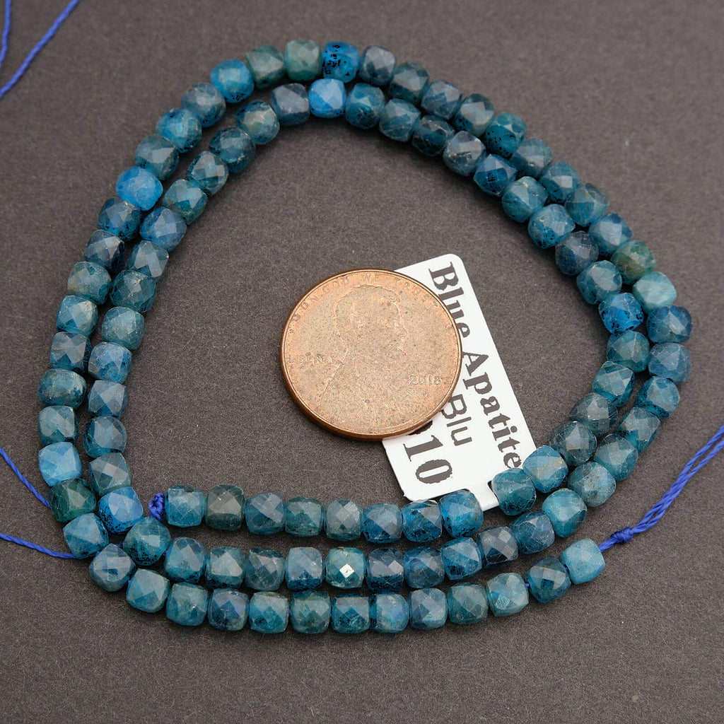 String of blue faceted beads with a coin for scale on a gray background