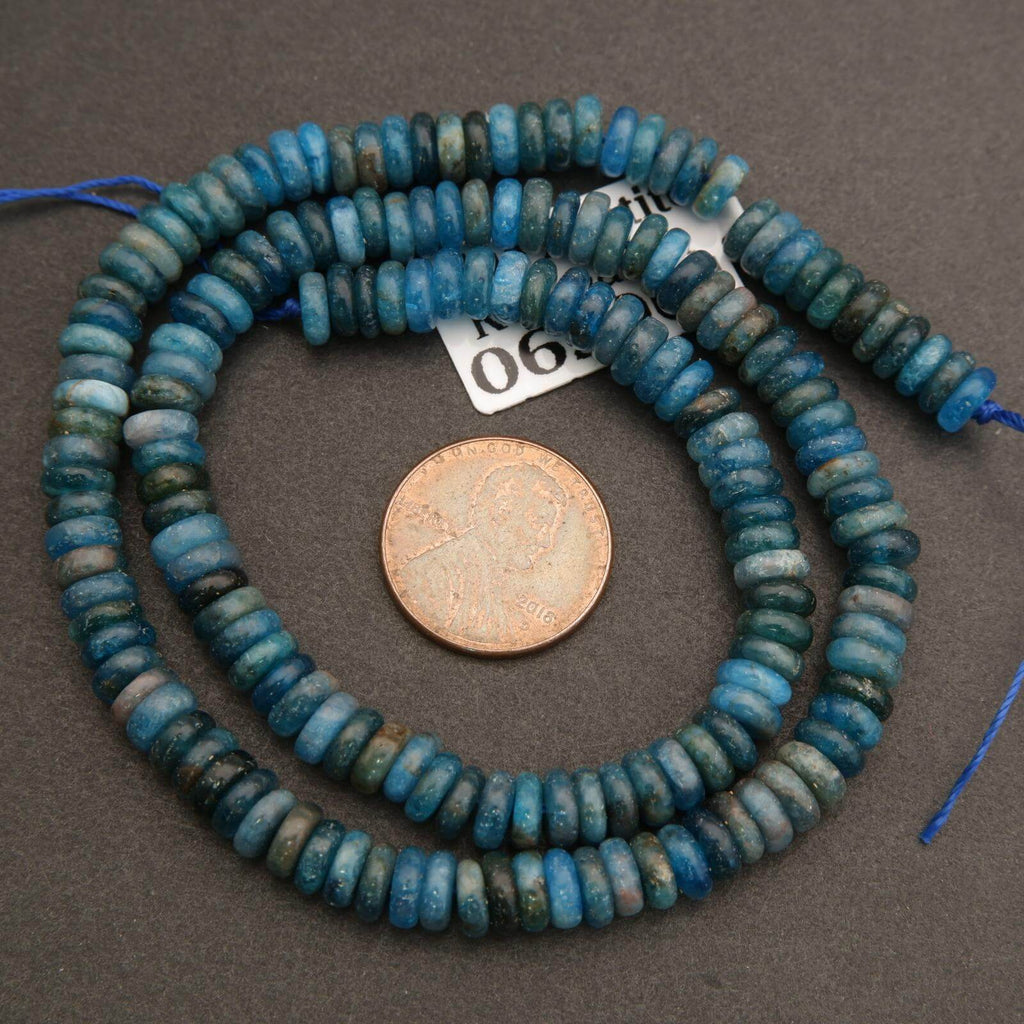 Blue glass beads with a penny for scale on a gray background