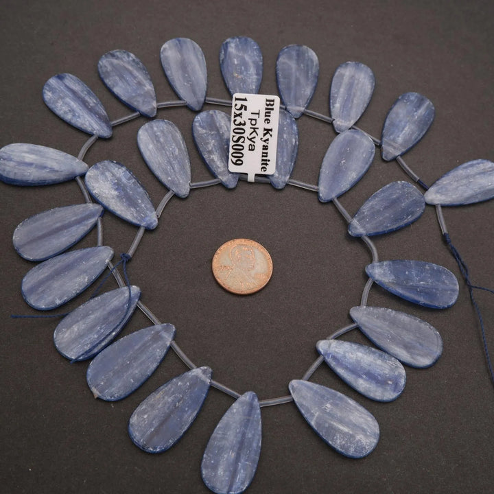 Blue teardrop beads arranged in a circular pattern with a penny for scale on a dark background.