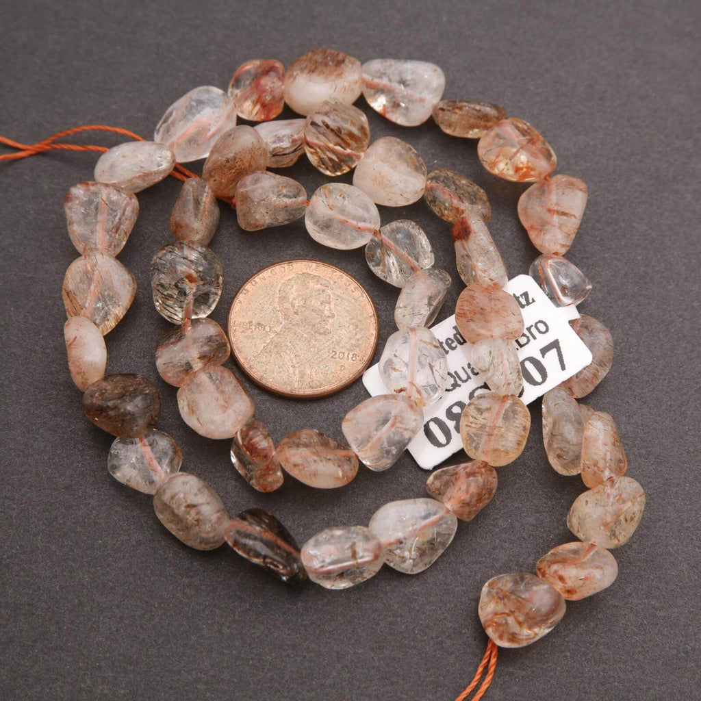 String of brown and clear gemstones with a penny for scale on a dark surface