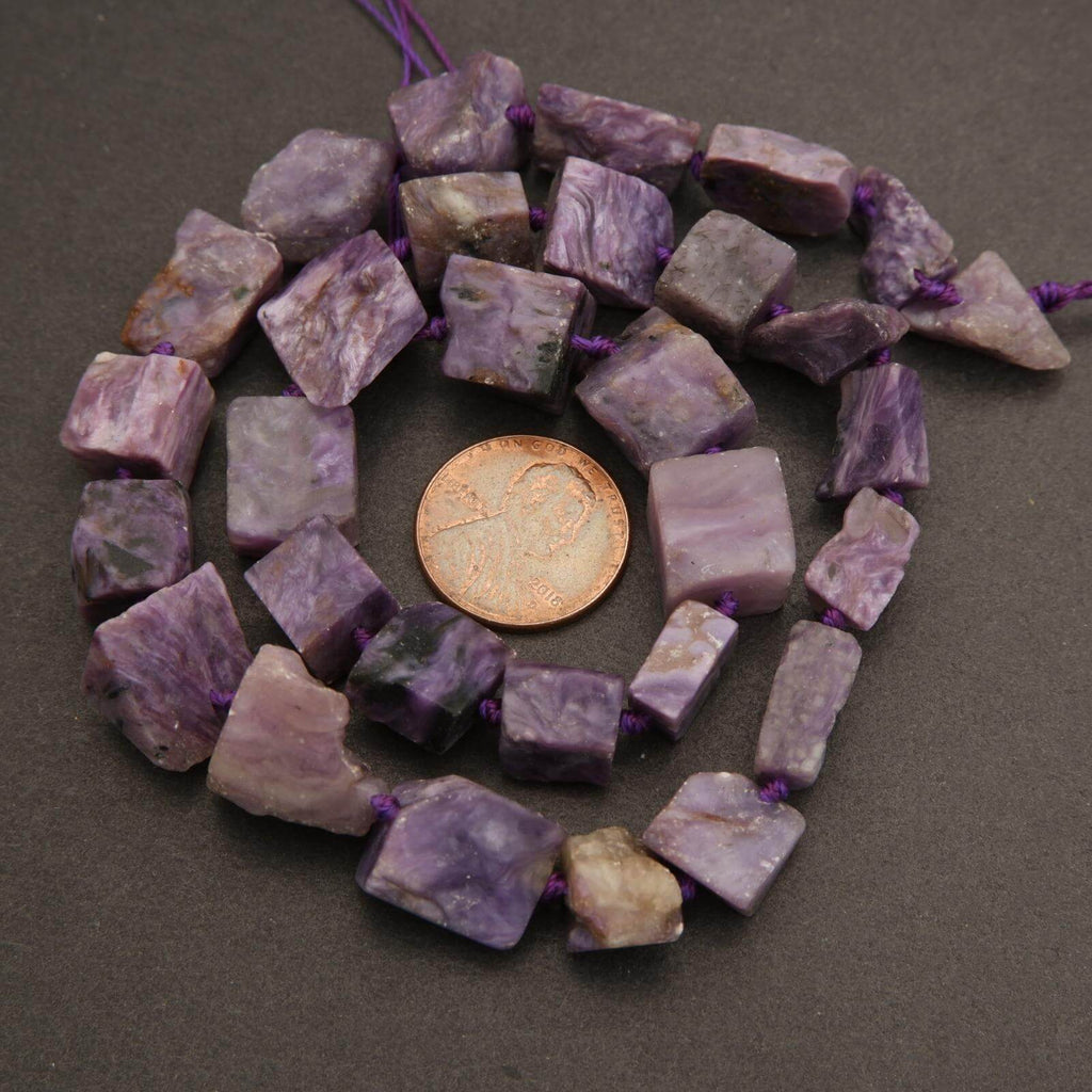 Necklace of purple and green beads with a coin for scale on a dark surface