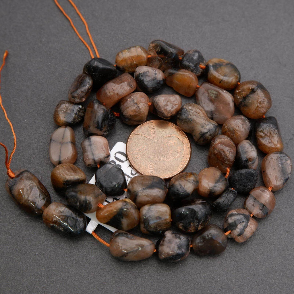 String of brown and black pebble beads with a penny for size reference on a gray background