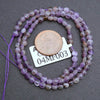 String of purple beads with a coin for scale on a gray background