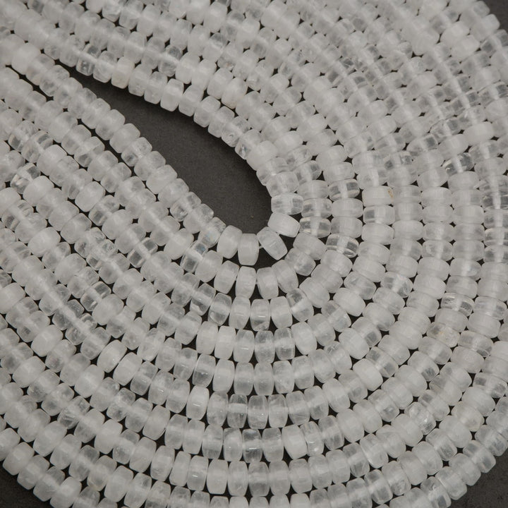 Assorted clear quartz heishi bead strands arranged in overlapping rows on a neutral background.