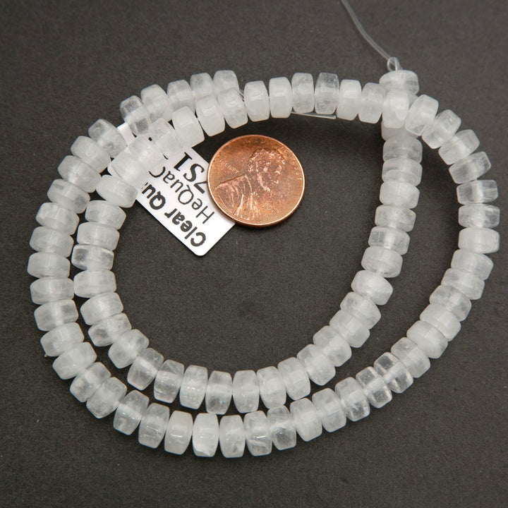Polished clear quartz heishi beads with translucent white appearance shown beside a penny for scale.