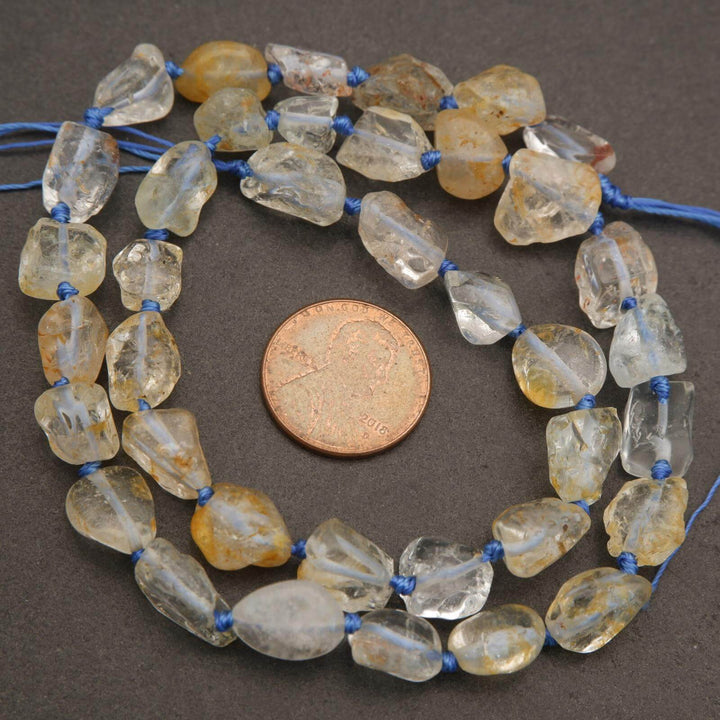 Necklace with yellowish beads and blue string next to a penny on a brown background