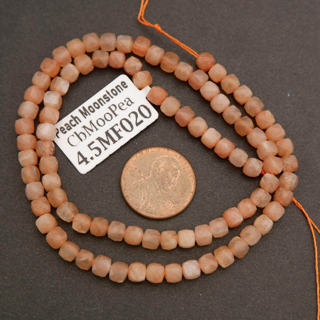 String of peach moonstone beads with a penny for scale on a dark surface