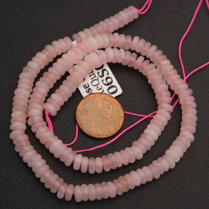 Pink beads on a string with a coin for scale on a black background