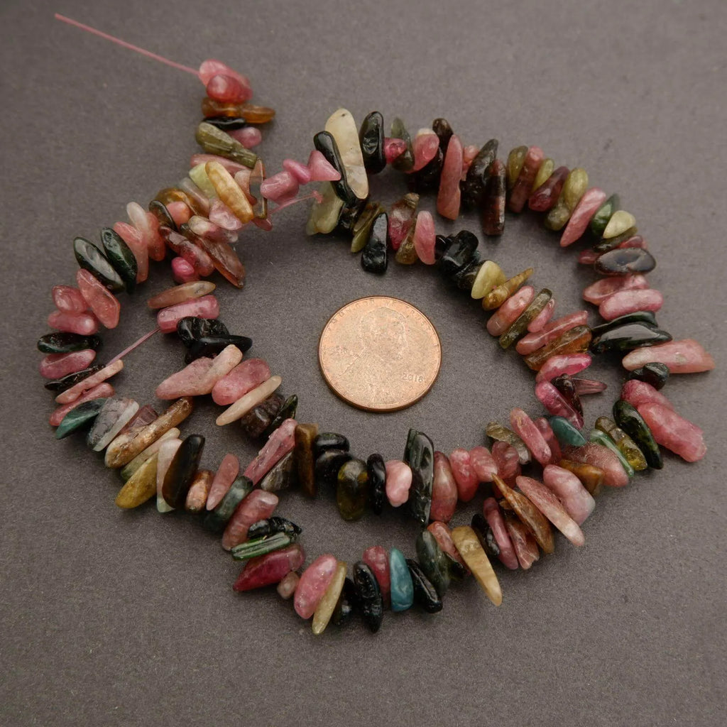 Necklace of multicolored stone beads with a coin for scale on a gray background