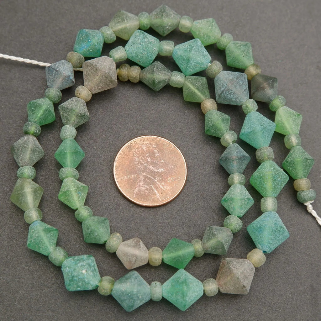 Necklace of green faceted beads with a penny for scale on a gray background