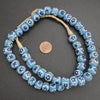 String of blue floral beads with a penny for scale on a gray background