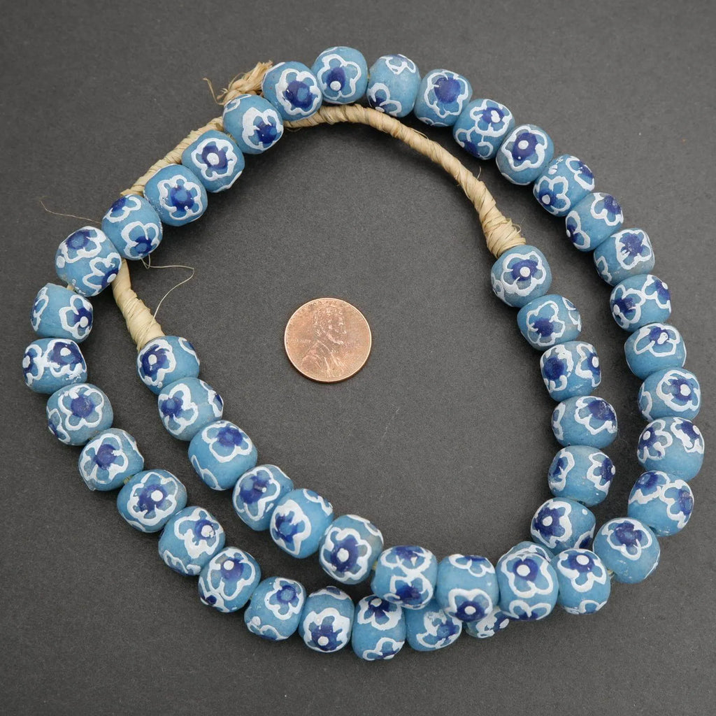 String of blue floral beads with a penny for scale on a gray background
