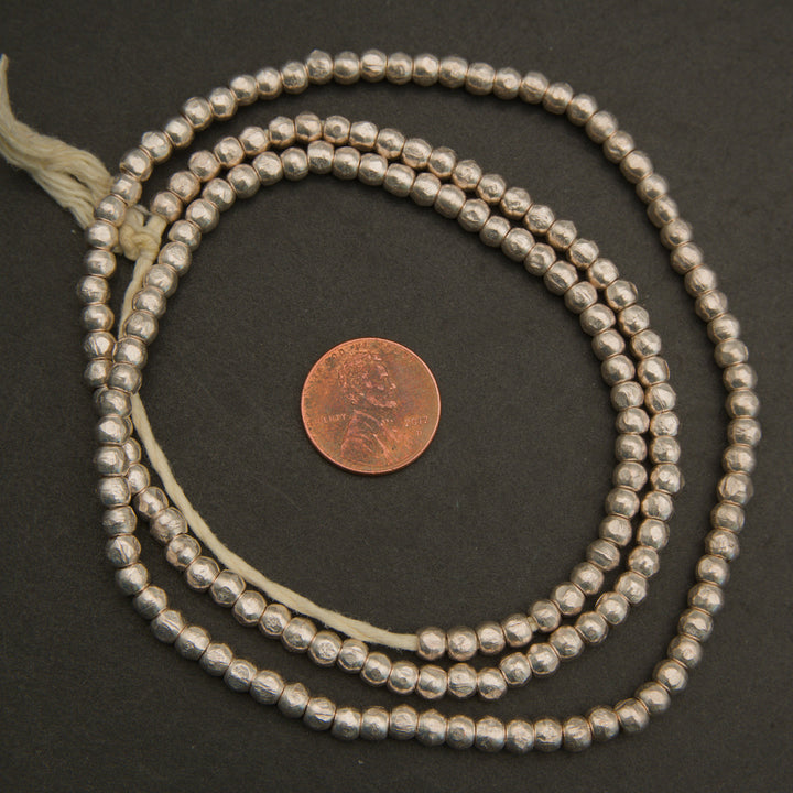 Silver beaded necklace with a penny for scale on a dark surface