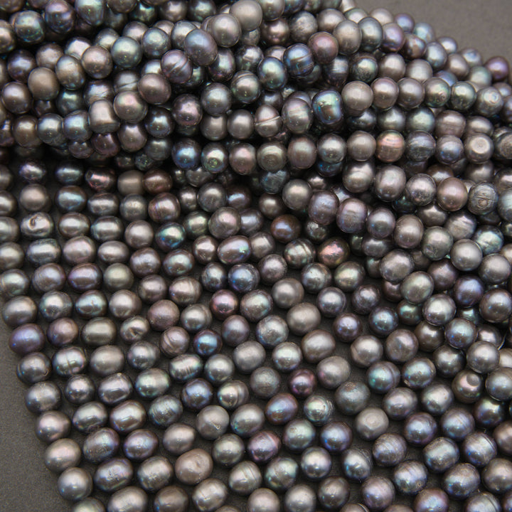 Strands of near-round peacock freshwater pearls fanned out on a gray background, with blue-green luster