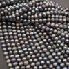 Strands of near-round peacock freshwater pearls fanned out on a gray background, with blue-green luster