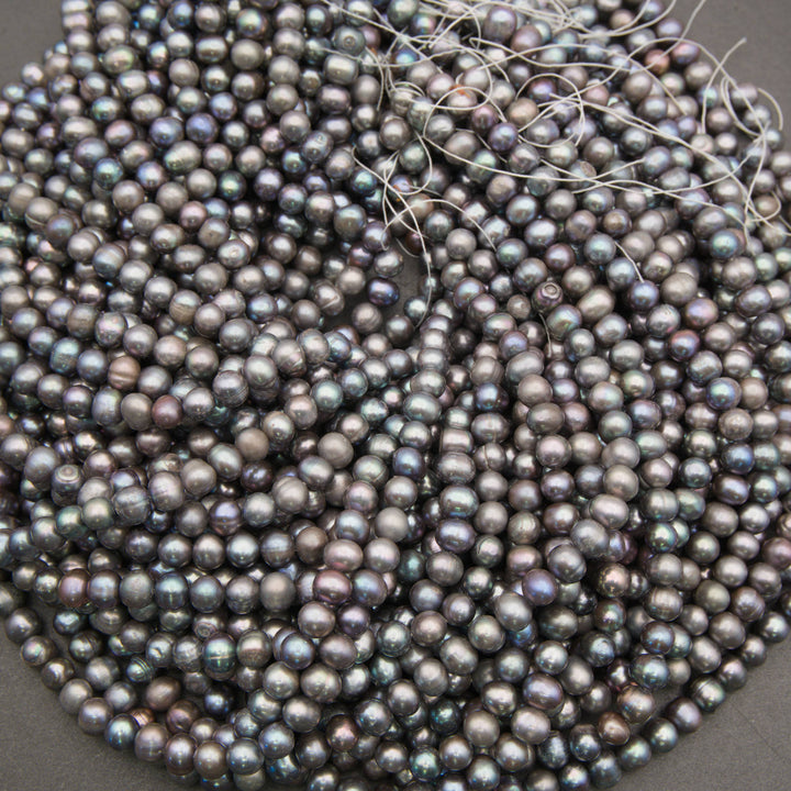 A heap of peacock freshwater pearl strands with loose thread ends, showing the range of gray, blue and purple tones
