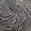 A heap of peacock freshwater pearl strands with loose thread ends, showing the range of gray, blue and purple tones
