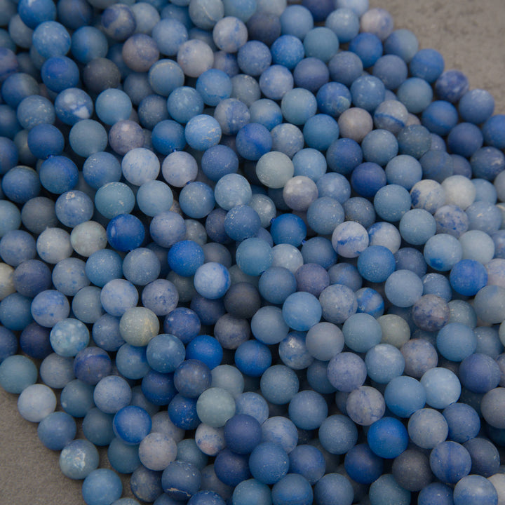 A heap of matte round dyed blue aventurine bead strands in denim blue and soft gray