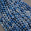 A heap of matte round dyed blue aventurine bead strands in denim blue and soft gray