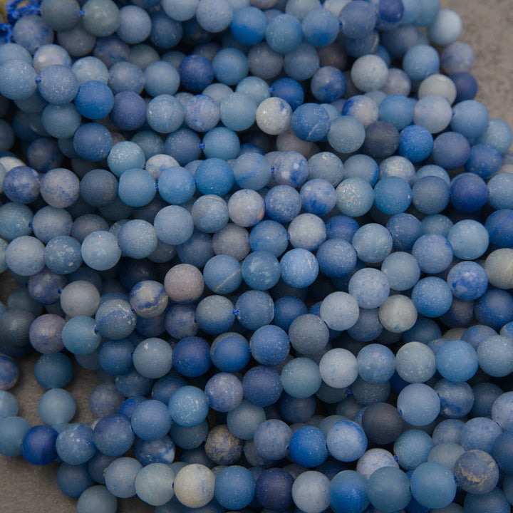 Strands of matte round dyed blue aventurine beads in rows on a gray background