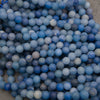 Strands of matte round dyed blue aventurine beads in rows on a gray background