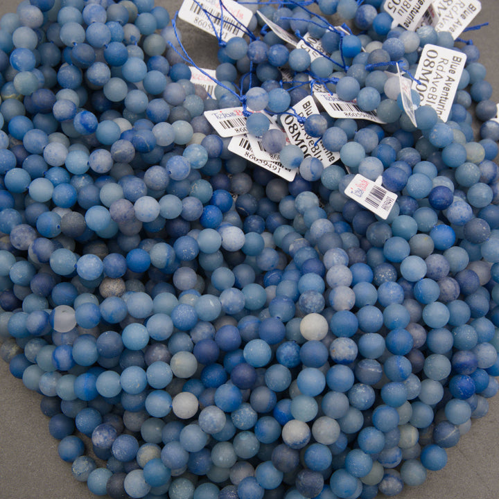 A bundle of matte round dyed blue aventurine bead strands with Tejas Beads tags