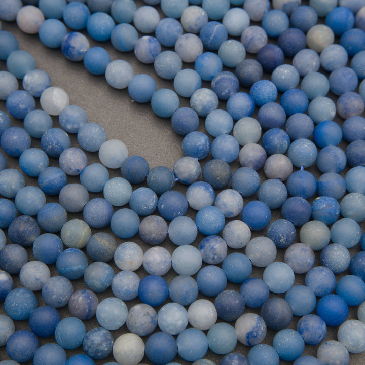 Rows of matte round dyed blue aventurine beads on a gray background in denim and pale blue