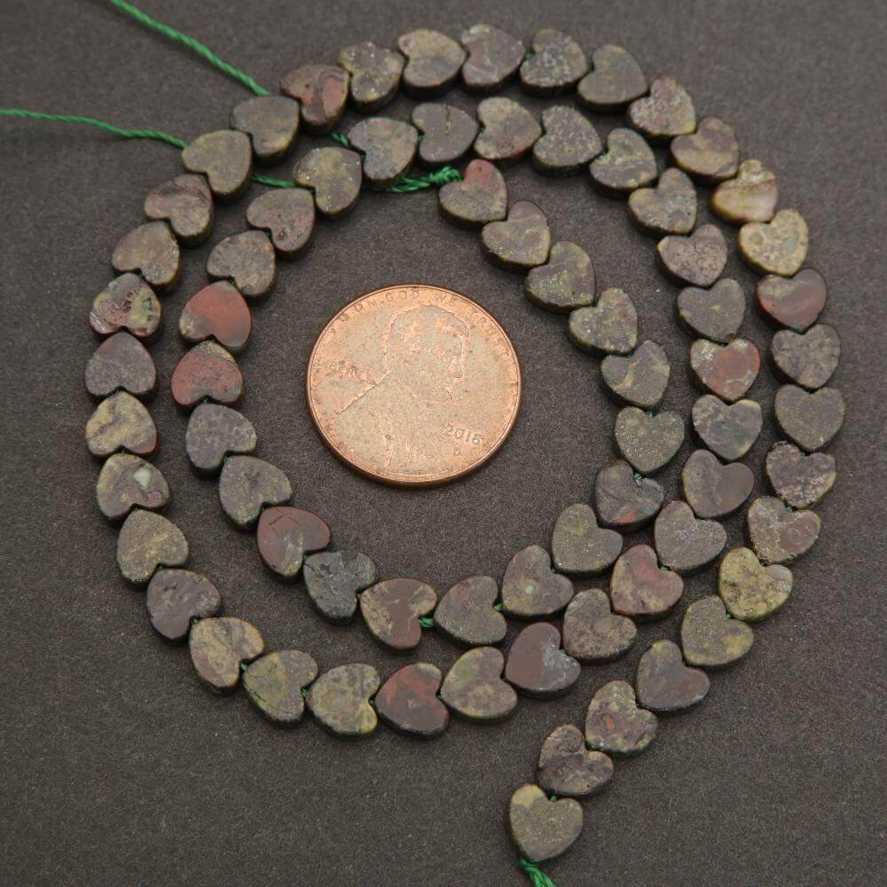 String of heart-shaped beads with a coin for scale on a dark background