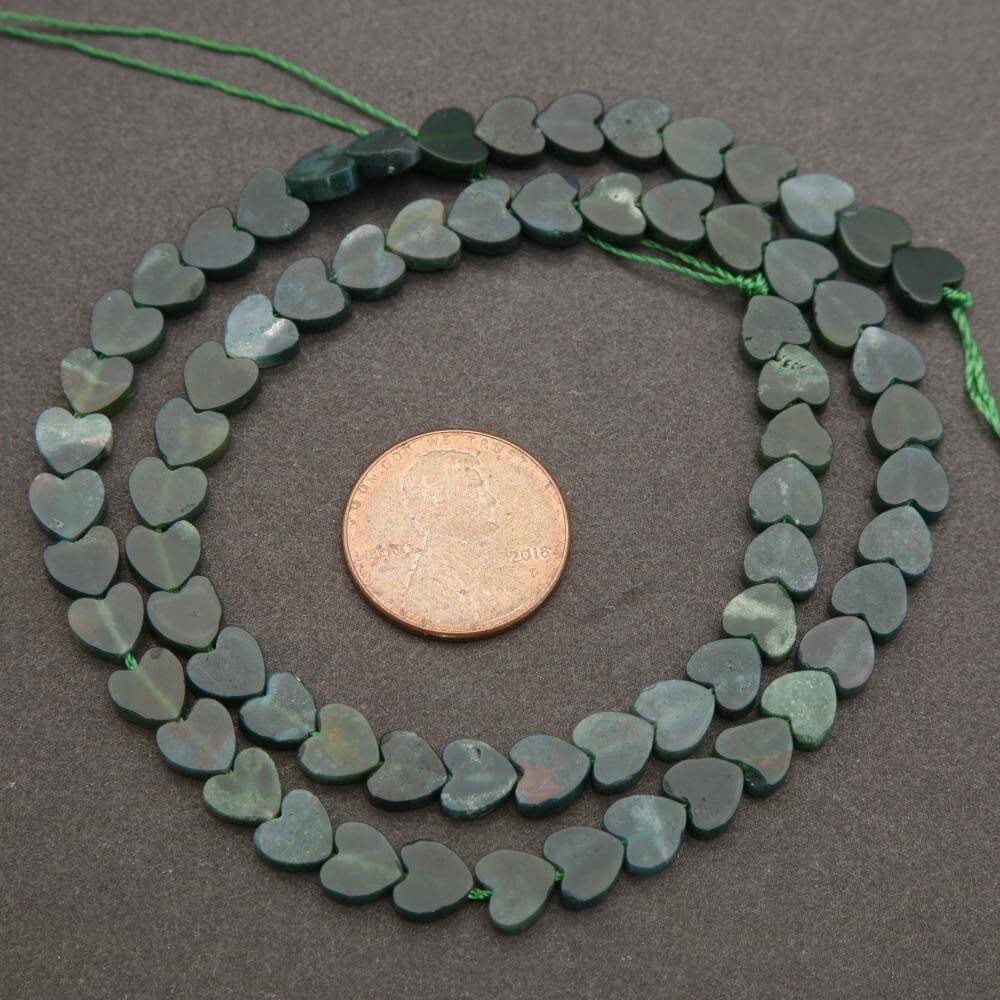 String of green heart-shaped beads with a penny for scale on a gray background