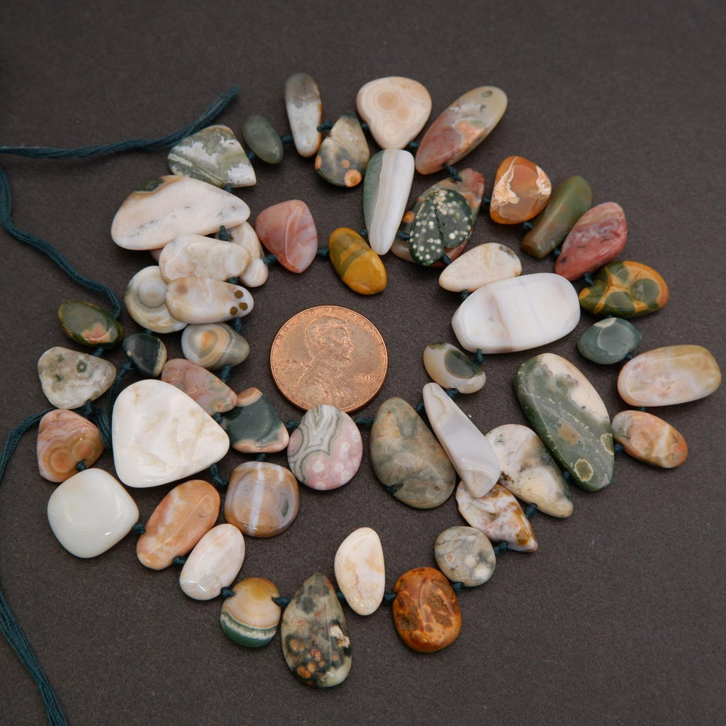 Assorted colorful stones arranged in a circular pattern on a dark surface with a penny in the center.