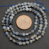 String of blue and gray beads with a penny for size comparison on a dark surface